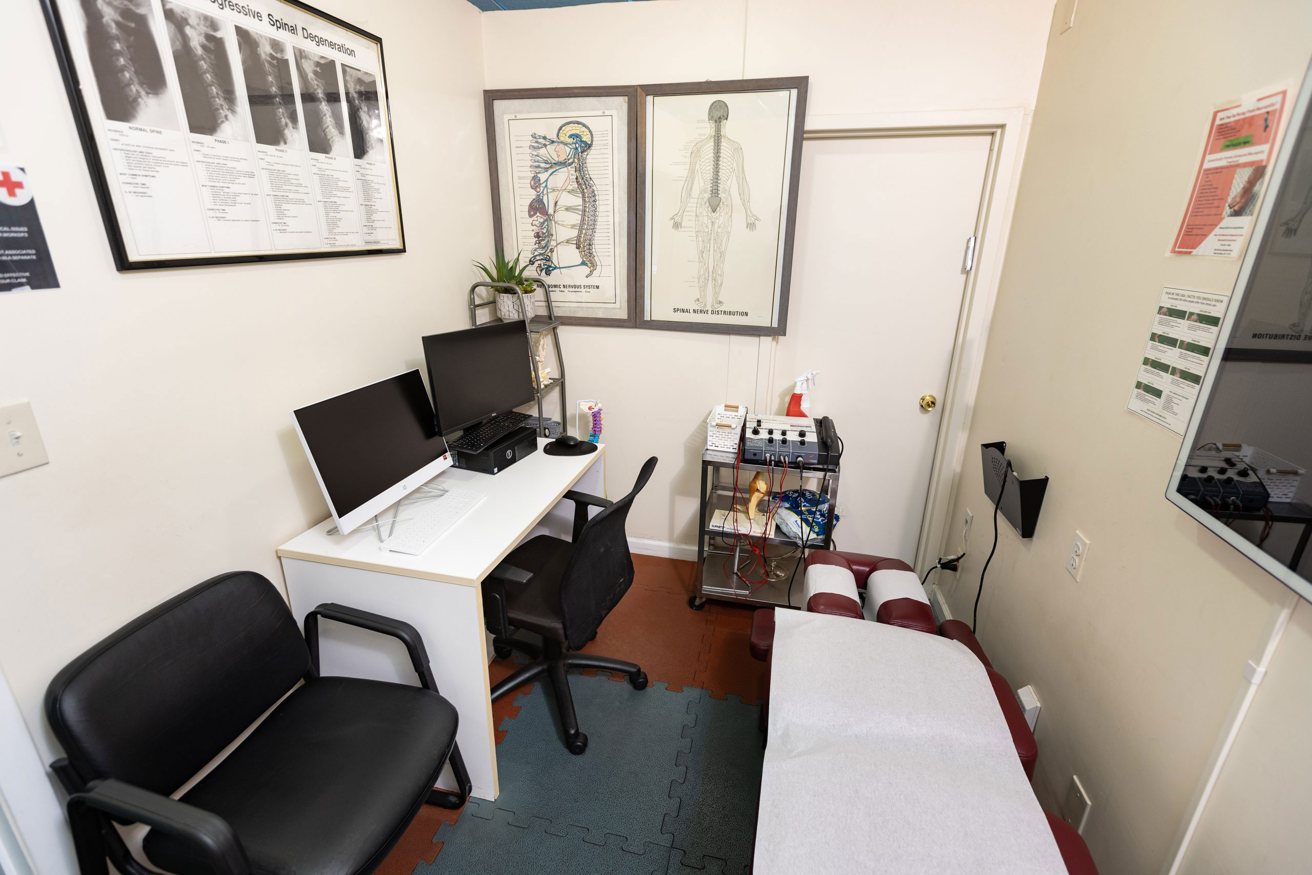 The image shows an interior view of a room with medical equipment, such as an X-ray machine, and a desk with a computer monitor, keyboard, and chair. There is also a small couch or chair in the corner.