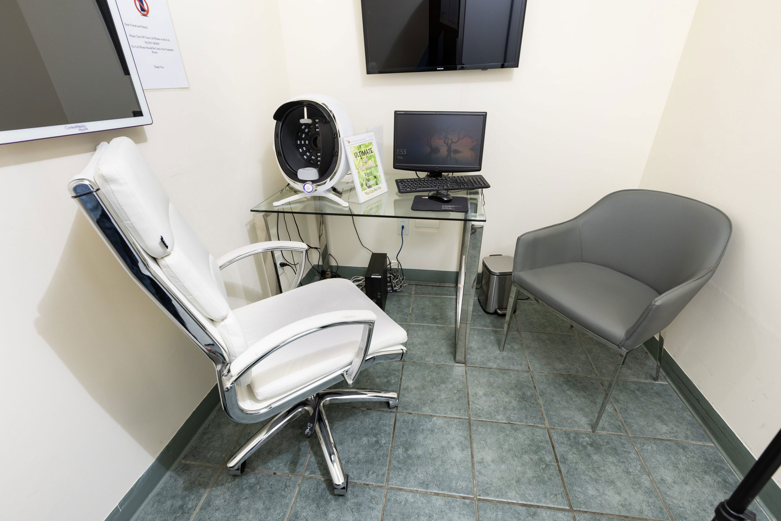 The image shows a dental office interior with various pieces of equipment, including a dental chair and a laptop on a desk, as well as a computer monitor.