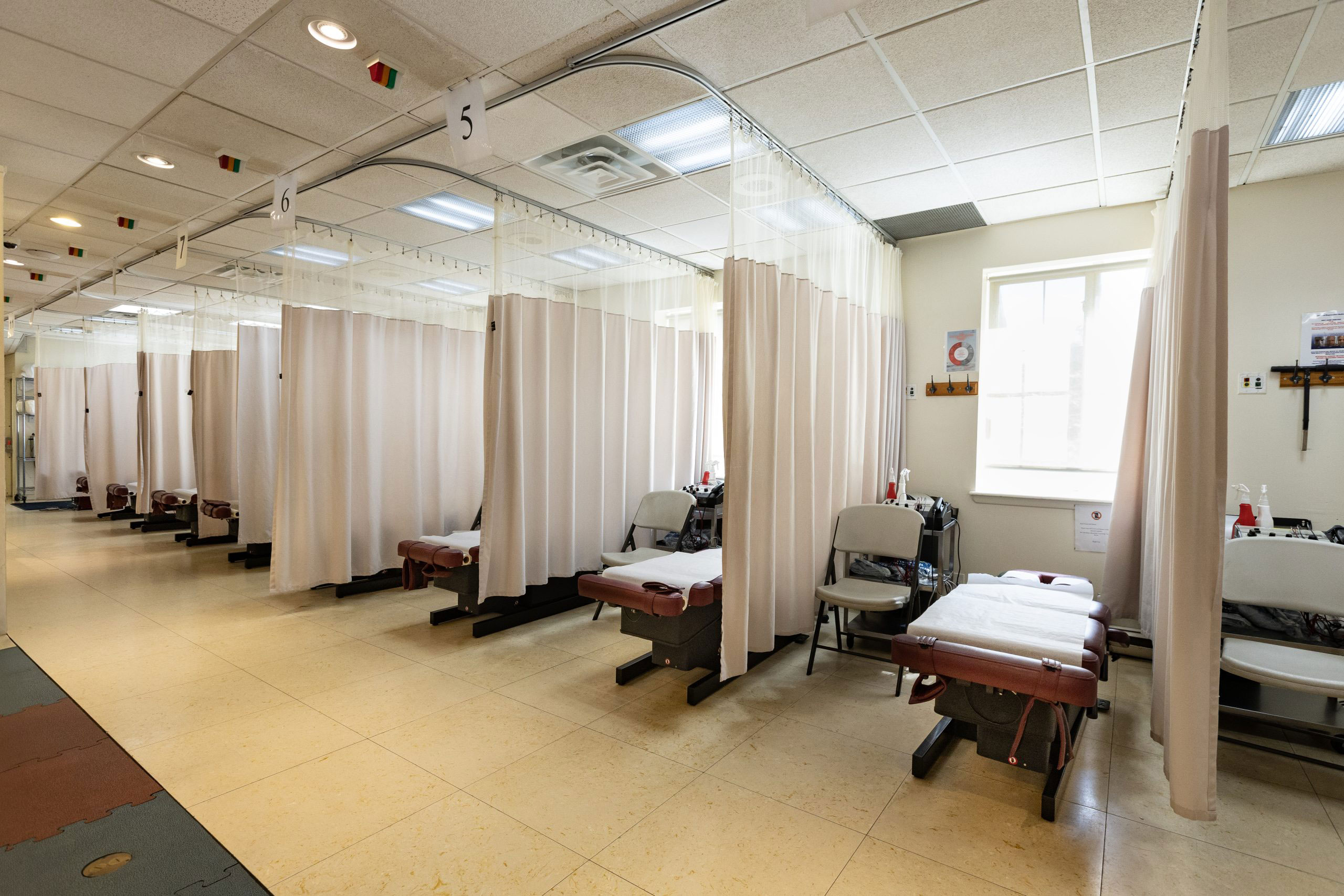 An interior view of a room with multiple examination tables and curtains, resembling a medical or dental office.