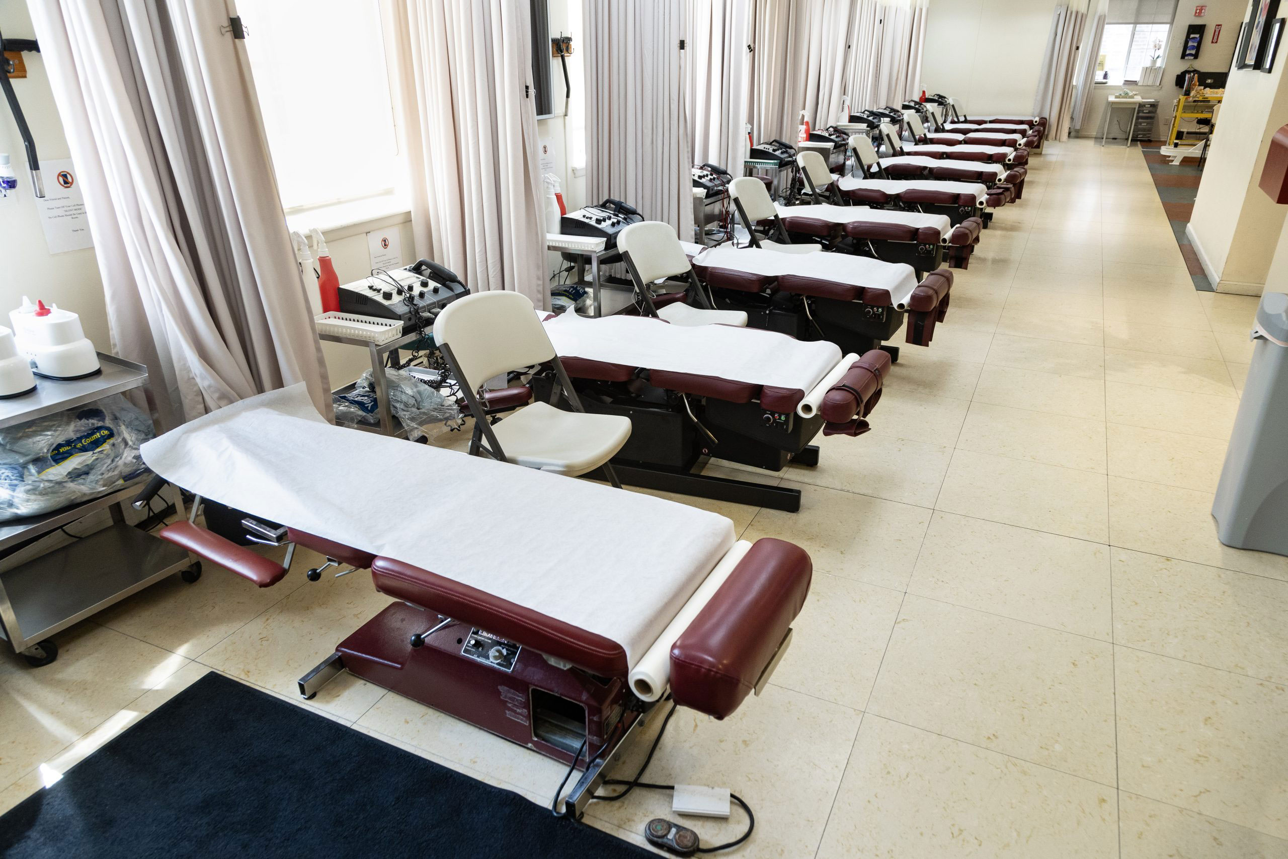 The image shows an interior view of a medical or dental office with several treatment tables lined up in a row, each covered with a white sheet.
