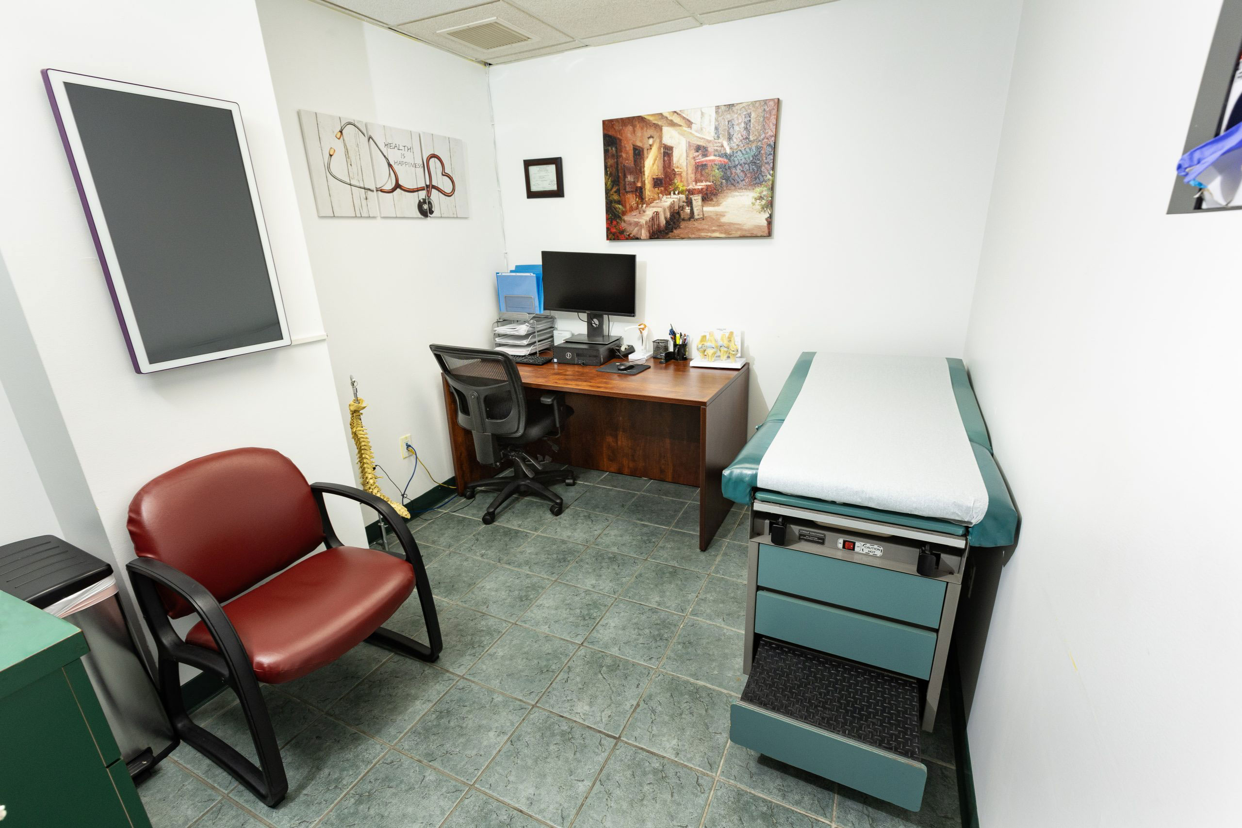 The image depicts a well-equipped medical office with a reception desk, a chair, a computer monitor, and various medical equipment.