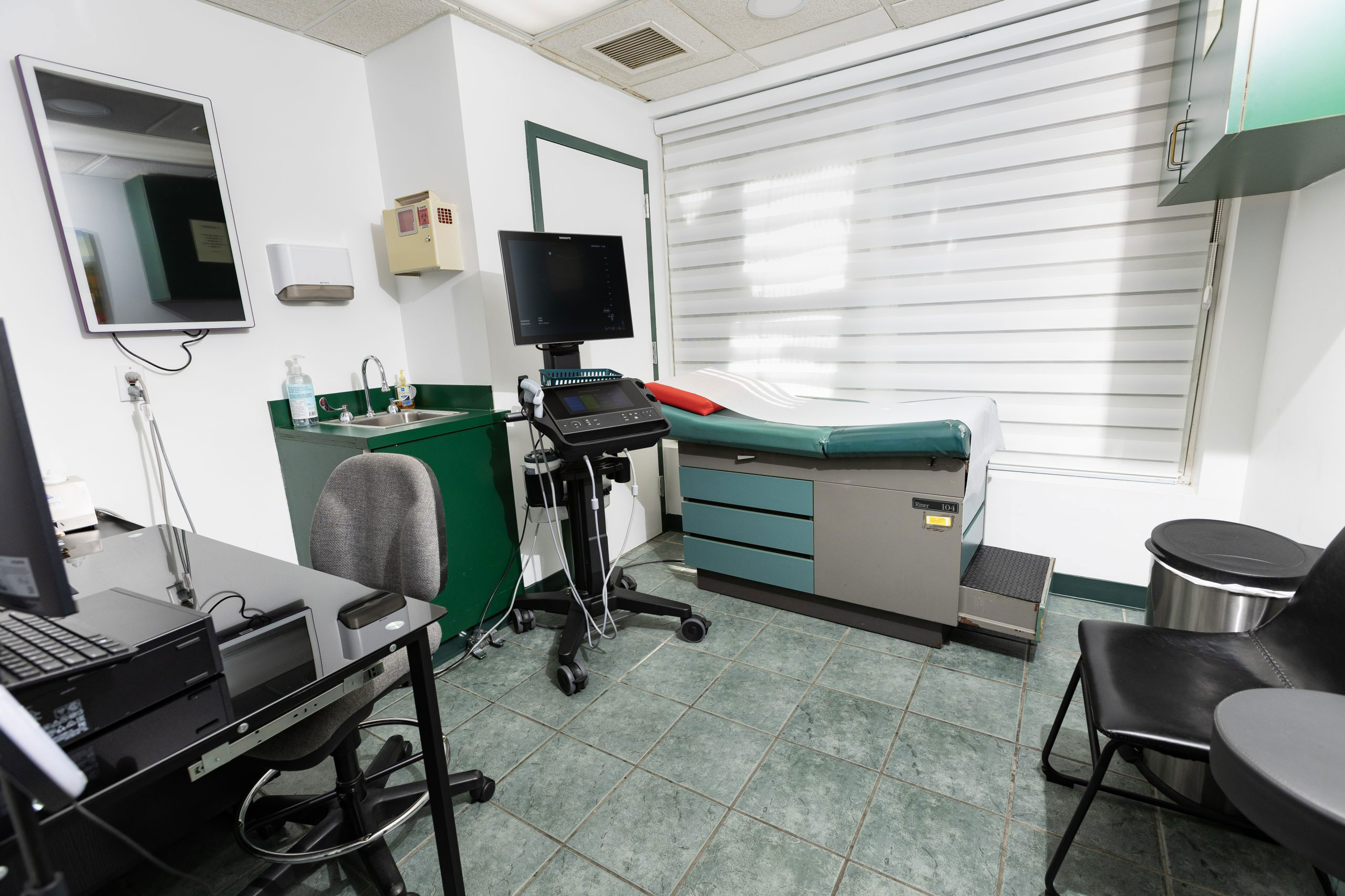 The image depicts an interior view of a medical or dental office, featuring a reception desk with chairs, a computer workstation, and various pieces of equipment typically found in such a setting.