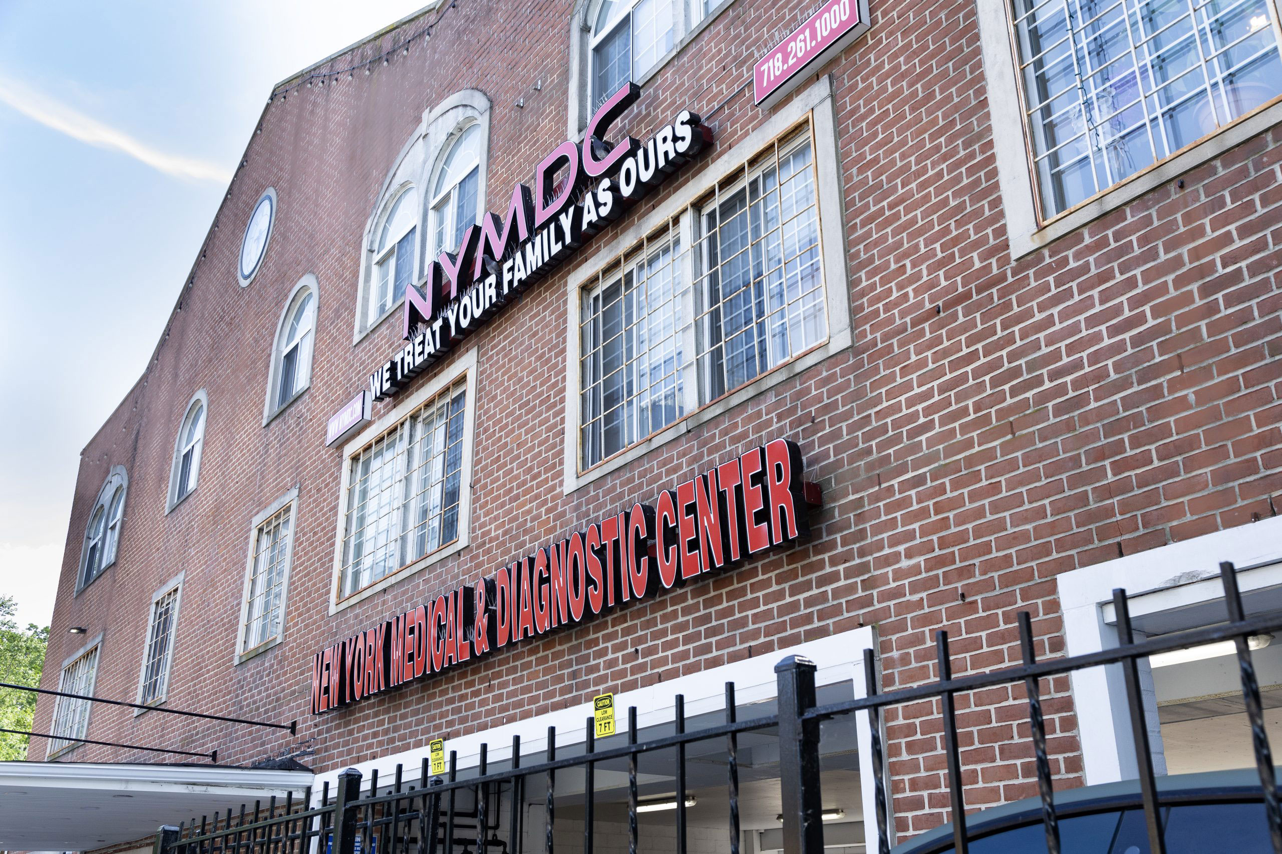 An image of a building with a sign that reads 'NYMDG' and other text, featuring a brick facade and a large window.