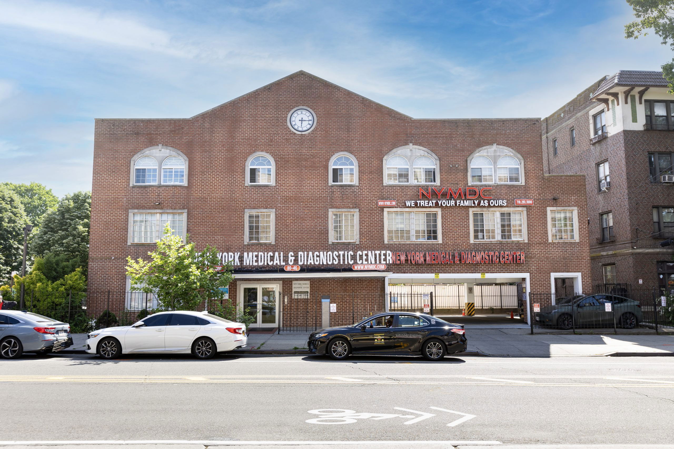 The image shows a large brick building with a sign that reads 'The Westwood Medical Center' and other text, indicating it is a medical facility. In front of the building, there are parked cars and a sidewalk with pedestrians.