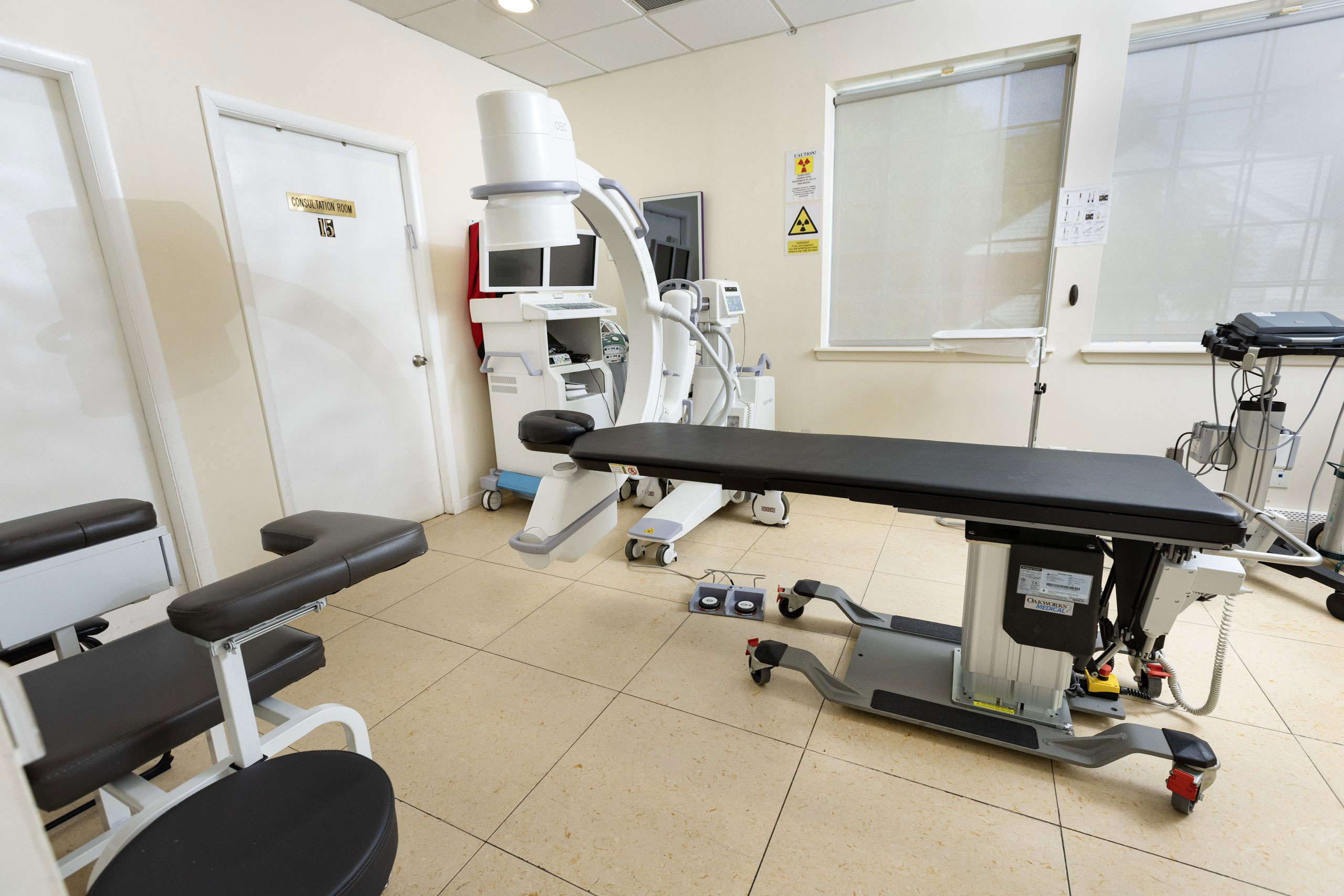 The image shows an interior view of a medical office with equipment and seating, including a dental chair and examination table.